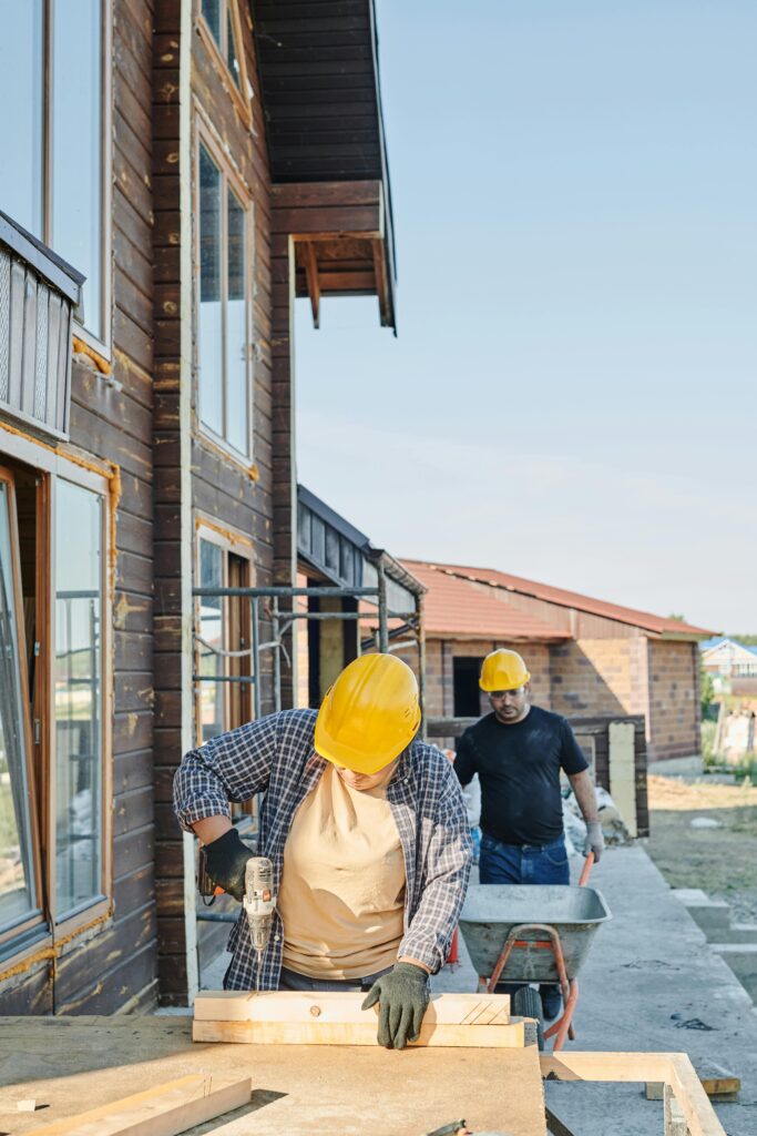 Two workers in hard hats engaged in carpentry at a construction site, building a wooden house.