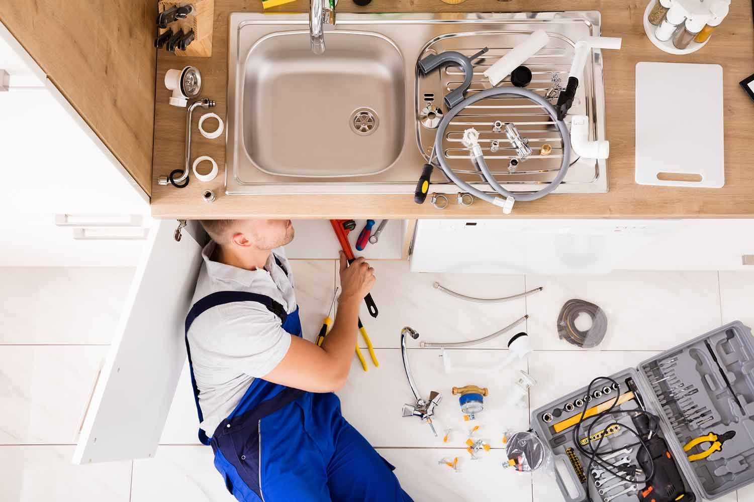 plumber working underneath kitchen sink with tools spread across the floor